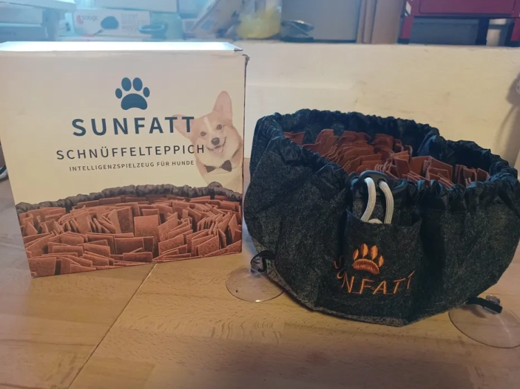 Szaro-brązowa okrągła mata węchowa dla psa Sunfatt o średnicy 30 cm obok fabrycznego kartonu