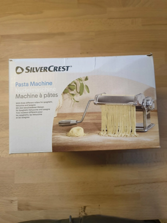 Biały karton z maszynką do makaronu Silvercrest Pasta Machine na drewnianym blacie