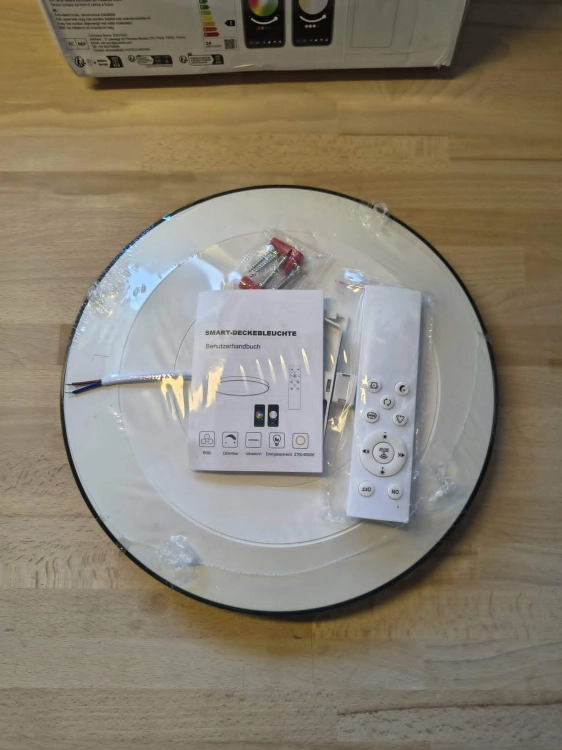 Czarna inteligentna lampa sufitowa LED plafon Smart Wi-Fi obok pilota i uszkodzonego kartonu