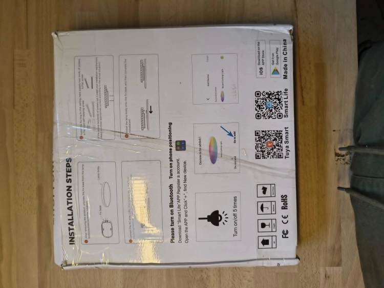 Czarna inteligentna lampa sufitowa LED plafon Smart Wi-Fi obok pilota i uszkodzonego kartonu