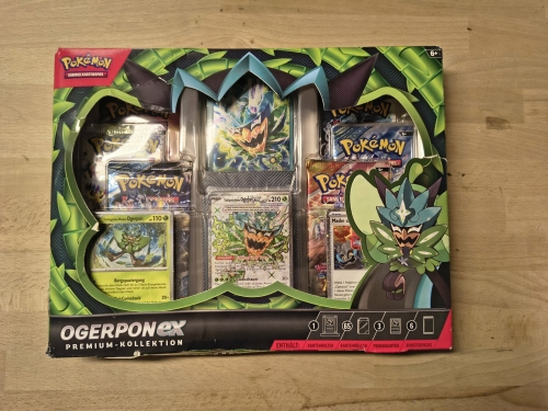 Nowy fabrycznie zamknięty zestaw Pokémon TCG Ogerpon ex Premium-Kollektion w niemieckiej wersji językowej z widocznymi boosterami i kartami promocyjnymi