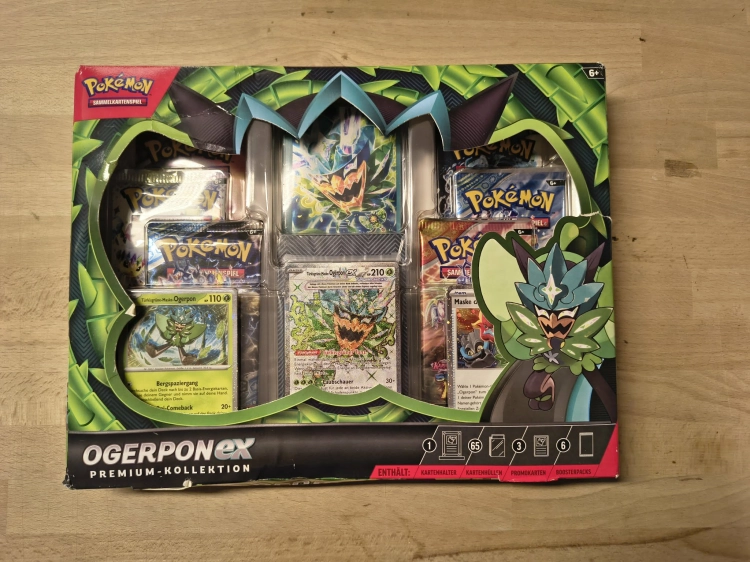 Nowy fabrycznie zamknięty zestaw Pokémon TCG Ogerpon ex Premium-Kollektion w niemieckiej wersji językowej z widocznymi boosterami i kartami promocyjnymi