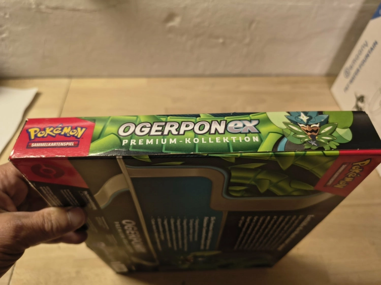 Nowy fabrycznie zamknięty zestaw Pokémon TCG Ogerpon ex Premium-Kollektion w niemieckiej wersji językowej z widocznymi boosterami i kartami promocyjnymi