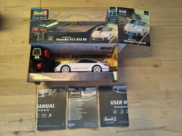 Nowe oryginalnie zapakowane białe zdalnie sterowane auto wyścigowe Revell Control Porsche 911 GT3 RS w skali 1 do 24 z widocznymi wgnieceniami na pudełku