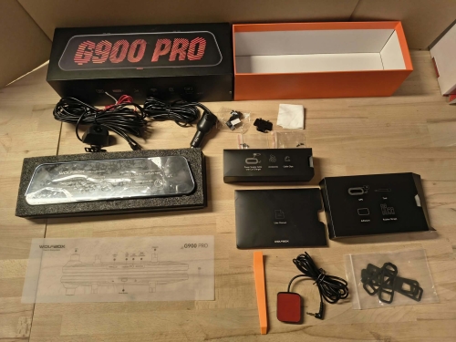 Nowy czarny wideorejestrator w lusterku WOLFBOX G900 Pro 4K rozpakowany z kompletem akcesoriów anteną GPS instrukcją i okablowaniem na drewnianym blacie