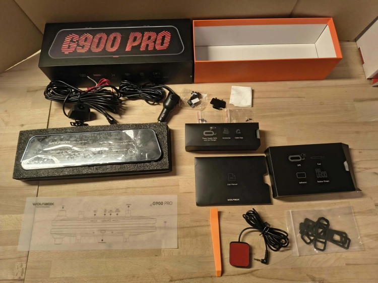 Nowy czarny wideorejestrator w lusterku WOLFBOX G900 Pro 4K rozpakowany z kompletem akcesoriów anteną GPS instrukcją i okablowaniem na drewnianym blacie