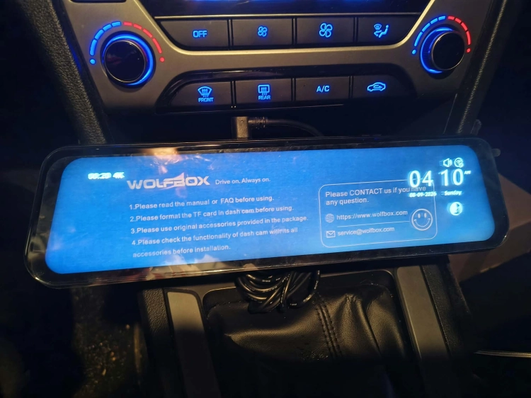 Nowy czarny wideorejestrator w lusterku WOLFBOX G900 Pro 4K rozpakowany z kompletem akcesoriów anteną GPS instrukcją i okablowaniem na drewnianym blacie