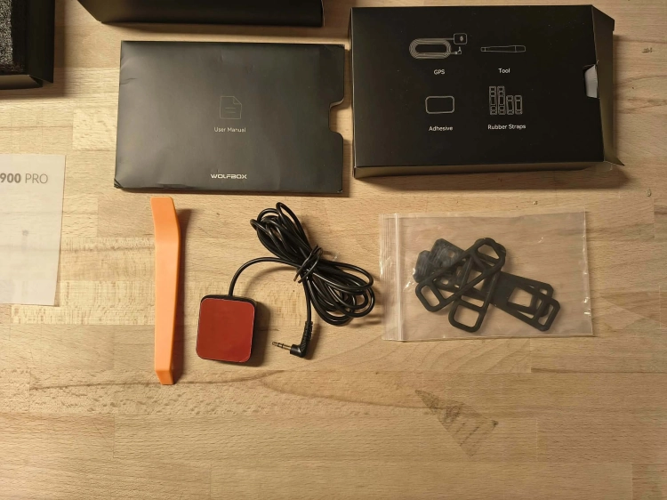 Nowy czarny wideorejestrator w lusterku WOLFBOX G900 Pro 4K rozpakowany z kompletem akcesoriów anteną GPS instrukcją i okablowaniem na drewnianym blacie