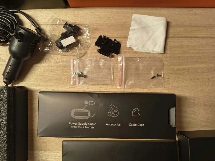 Nowy czarny wideorejestrator w lusterku WOLFBOX G900 Pro 4K rozpakowany z kompletem akcesoriów anteną GPS instrukcją i okablowaniem na drewnianym blacie