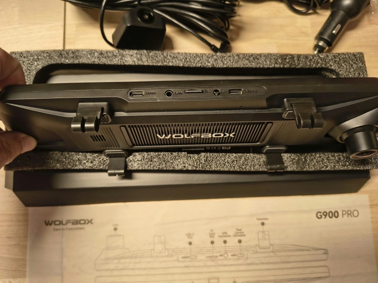 Nowy czarny wideorejestrator w lusterku WOLFBOX G900 Pro 4K rozpakowany z kompletem akcesoriów anteną GPS instrukcją i okablowaniem na drewnianym blacie
