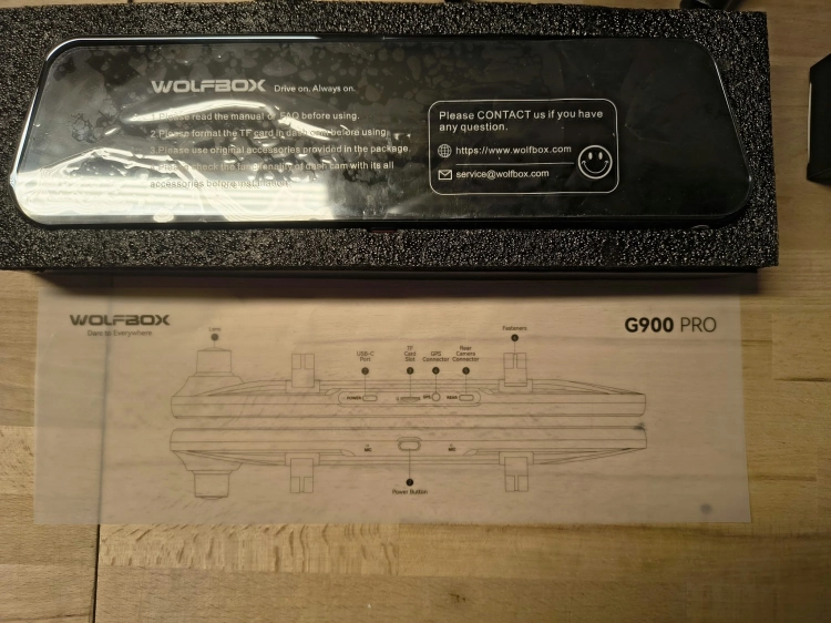 Nowy czarny wideorejestrator w lusterku WOLFBOX G900 Pro 4K rozpakowany z kompletem akcesoriów anteną GPS instrukcją i okablowaniem na drewnianym blacie