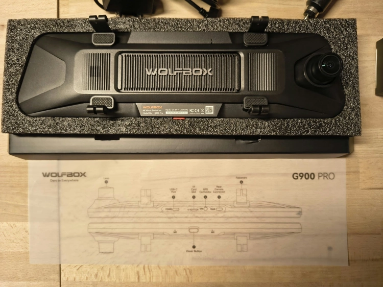 Nowy czarny wideorejestrator w lusterku WOLFBOX G900 Pro 4K rozpakowany z kompletem akcesoriów anteną GPS instrukcją i okablowaniem na drewnianym blacie