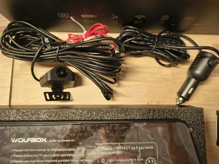 Nowy czarny wideorejestrator w lusterku WOLFBOX G900 Pro 4K rozpakowany z kompletem akcesoriów anteną GPS instrukcją i okablowaniem na drewnianym blacie