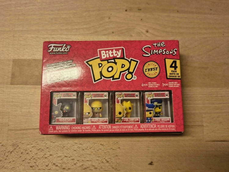 Nowy oryginalnie zapakowany zestaw czterech figurek Funko Bitty Pop The Simpsons z postaciami Scratchy Grampa Lisa i Chief Wiggum na drewnianym stole